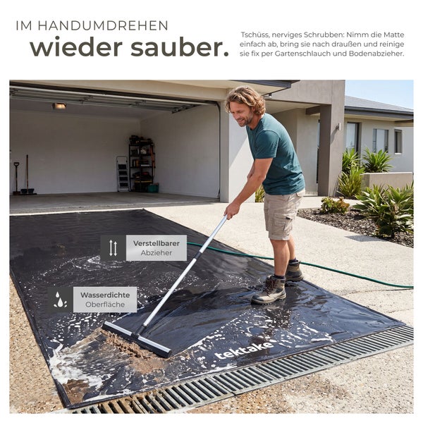 Ein Mann reinigt eine wasserdichte Garagenmatte von tektake mit einem verstellbaren Bodenabzieher im hellen Außenbereich vor einer Garage.