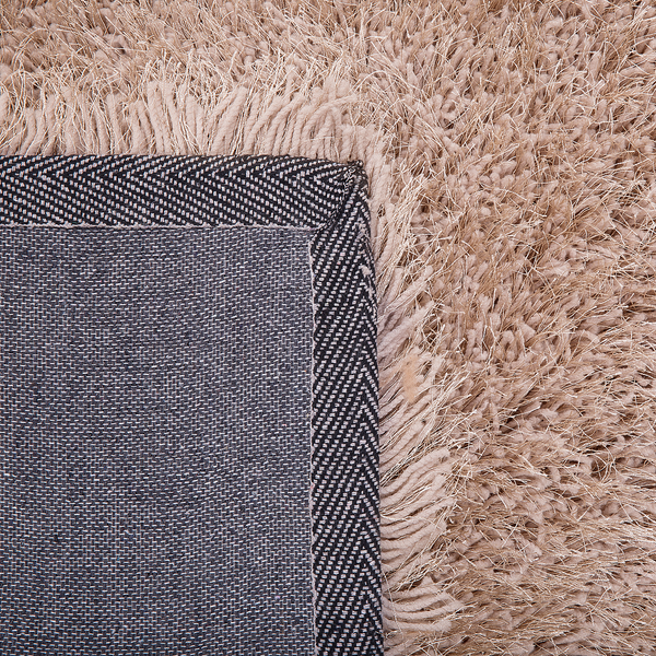 Nahaufnahme eines beige Hochflor-Teppichs mit sichtbarer strukturierter Rückseite.