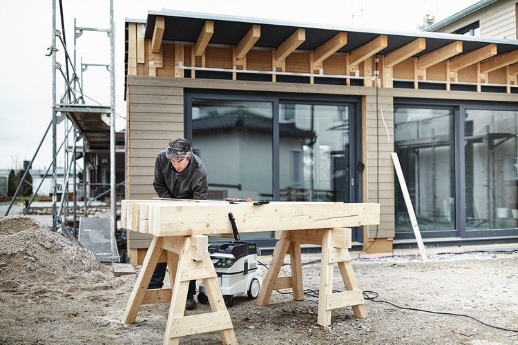 Handwerker bei der Holzbearbeitung auf einer Baustelle mit Unterstellböcken, Bauholz und einem Industriesauger