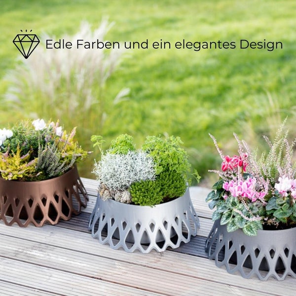 Drei dekorative Pflanzgefäße aus Metall mit Pflanzen auf einer Holzterrasse.