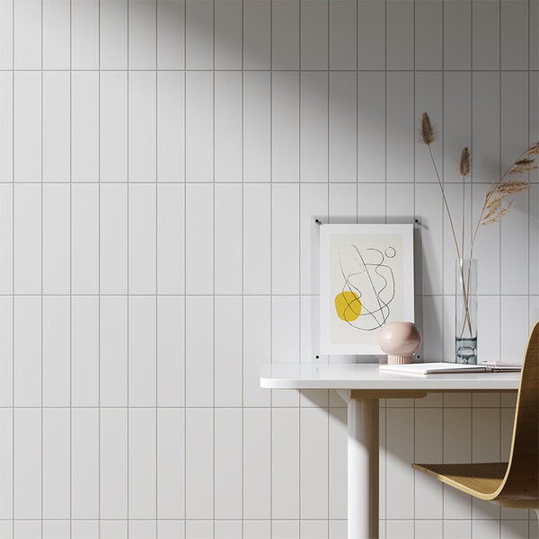 Wandfliesen im Rechteckformat an einer Innenwand, kombiniert mit einem modernen Schreibtisch, einer Vase mit Gräsern und einem abstrakten Bild.