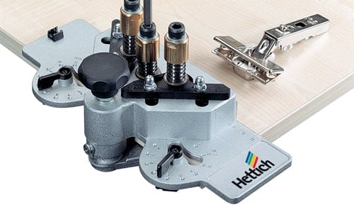 Hettich Bohrlehre für Scharniere auf einer Holzplatte mit Topfscharnier, Hettich Logo.
