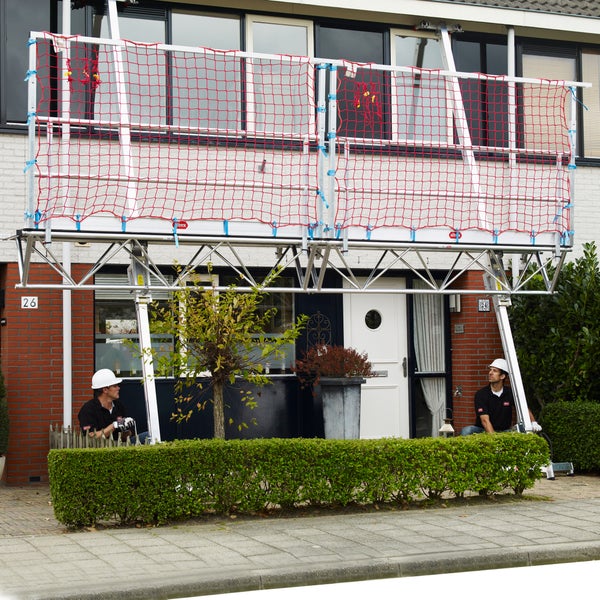 Altrex Dachkantensicherung mit Auffangnetz und Aluminiumrahmen vor einer Hausfassade montiert.