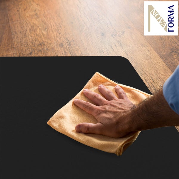 Eine Hand reinigt eine schwarze Bodenschutzmatte mit einem Tuch auf einem Holzboden. Nova Forma Logo.