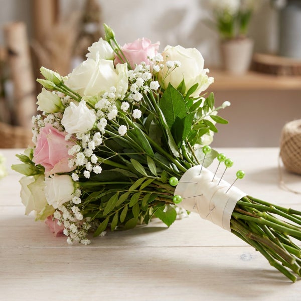Ein Blumenstrauß mit Rosen und Schleierkraut auf einem Holztisch, gebunden mit einem Satinband und verzierten Stecknadeln.