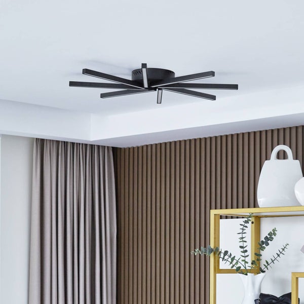 Moderne schwarze Deckenleuchte im Sterndesign in einem hellen Raum mit Holzlamellenwand und Vorhängen.