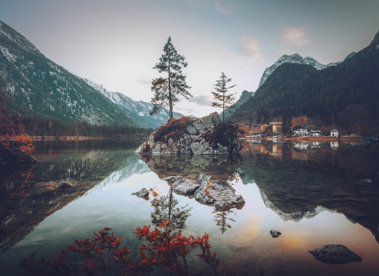 Wandbild mit Bergsee, kleiner Felsinsel mit zwei Bäumen, Spiegelung im klaren Wasser und schneebedeckten Bergen im Hintergrund.