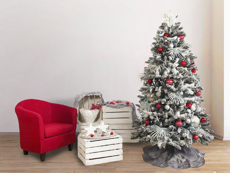 Geschmückter, beschneiter künstlicher Weihnachtsbaum neben einem Sessel und Holzkisten als weihnachtliche Dekoration im Innenbereich.