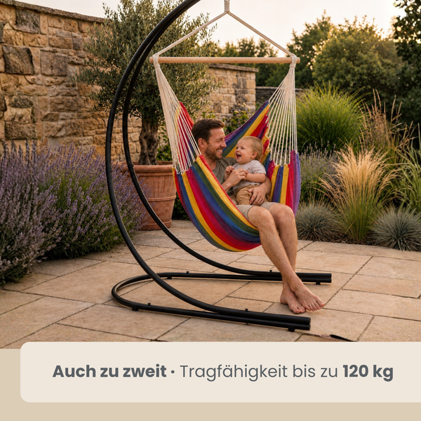 Vater mit Kind im bunten Hängesessel mit schwarzem Metallgestell auf einer Steinterrasse im Garten