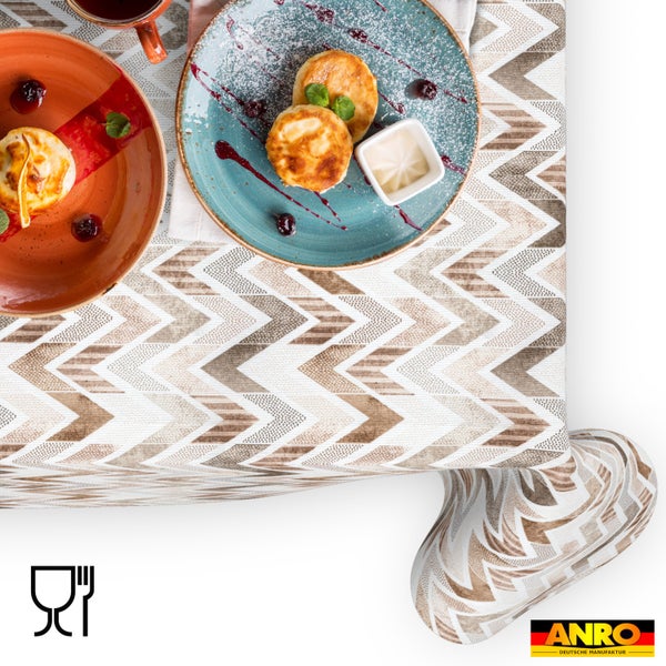 Tischdecke mit Zickzack-Muster in Beige und Braun, gedeckter Frühstückstisch mit Tellern. ANRO Logo und Symbol für Lebensmittelechtheit.
