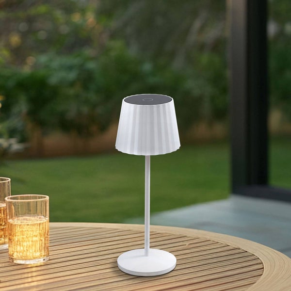Moderne weiße Solar-Tischleuchte mit plissiertem Schirm auf einem runden Holztisch im Garten.