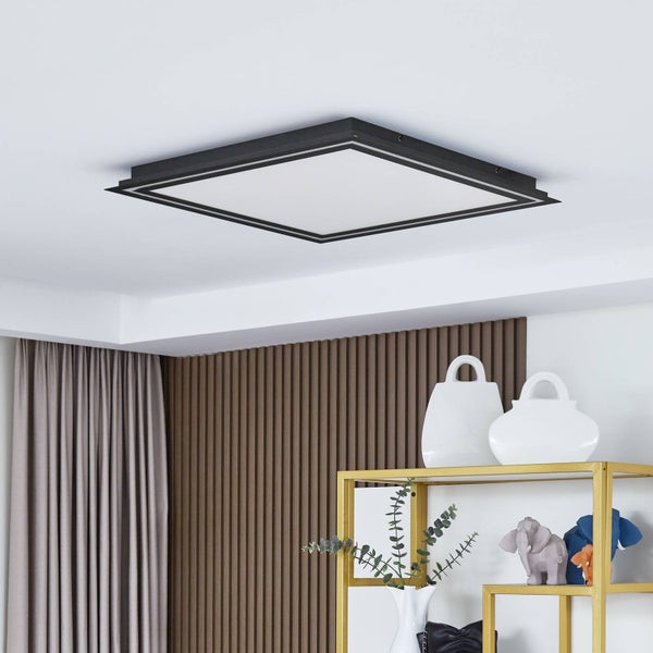 Quadratisches LED-Panel mit schwarzem Rahmen an einer weißen Zimmerdecke über einem modernen Regal mit Dekoration.