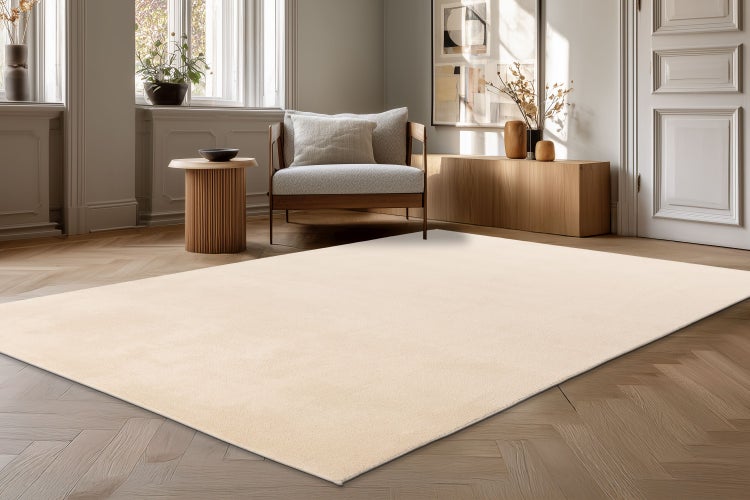 Ein unifarbener, flauschiger Teppich in einem modern eingerichteten Wohnzimmer mit Parkettboden und einem Sessel.