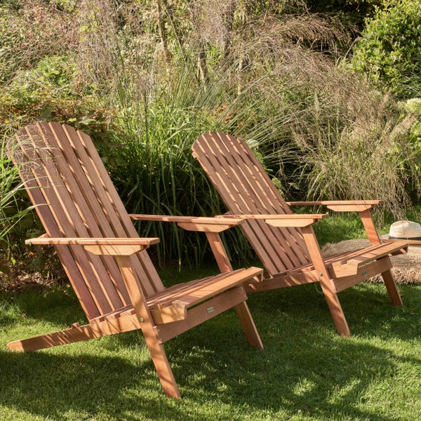 Zwei Adirondack-Gartenstühle aus Holz auf einer Rasenfläche vor hohen Gräsern in einem hellen Garten.