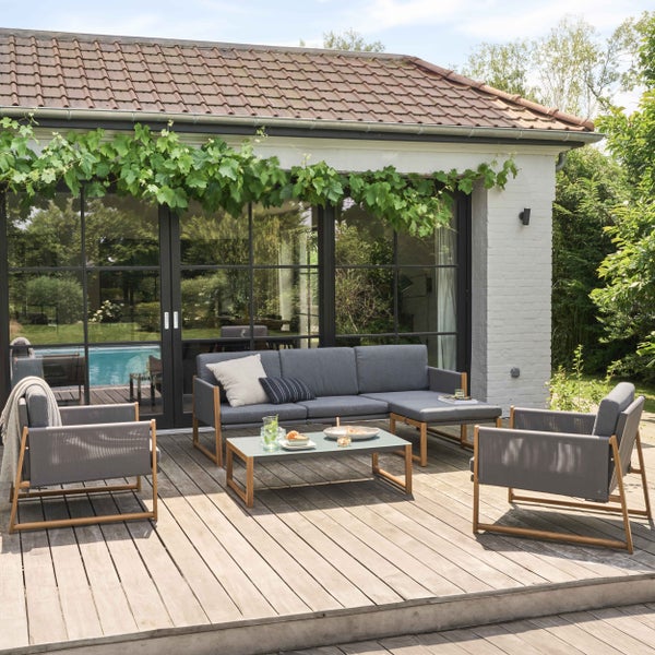 Helle, moderne Gartenlounge aus Holz mit grauen Polstern auf einer Holzterrasse mit Sofa, Sesseln und Couchtisch.