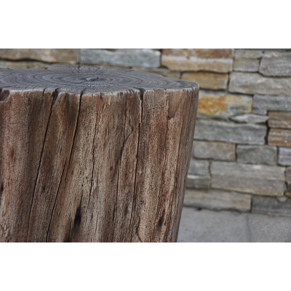Dekorativer Gartenhocker in realistischer Baumstumpf-Optik mit ausgeprägter Holzmaserung und Jahresringen vor einer Steinmauer.