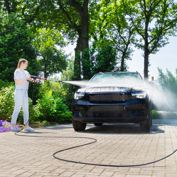 Frau reinigt Auto mit Hochdruckreiniger im Freien
