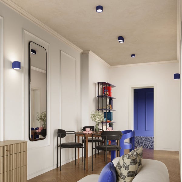 Heller, moderner Wohnbereich mit rundem Esstisch, schwarzen Stühlen, blauen Wand- und Deckenleuchten, Wandspiegel und Parkettboden.