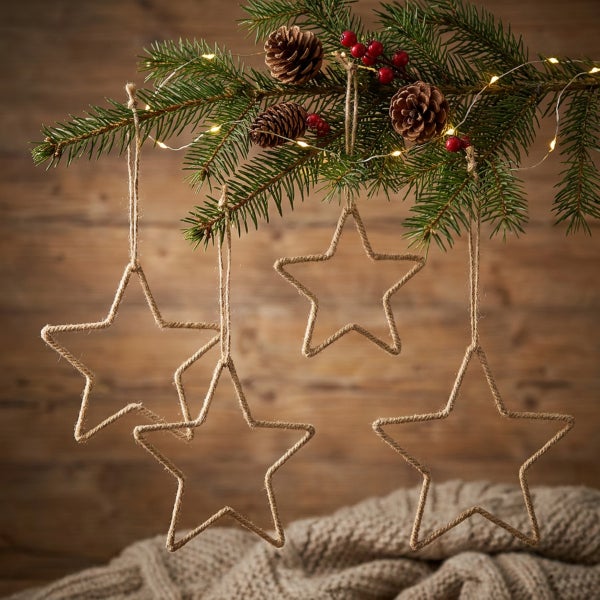 Vier weihnachtliche Hängesterne aus Juteschnur hängen an einem Tannenbaumzweig mit Lichterkette, Zapfen und roten Beeren.