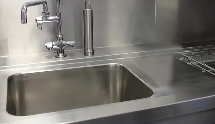 Edelstahlspüle mit integrierter Küchenarmatur und Arbeitsplatte aus Metall in einer professionellen Küchenumgebung.