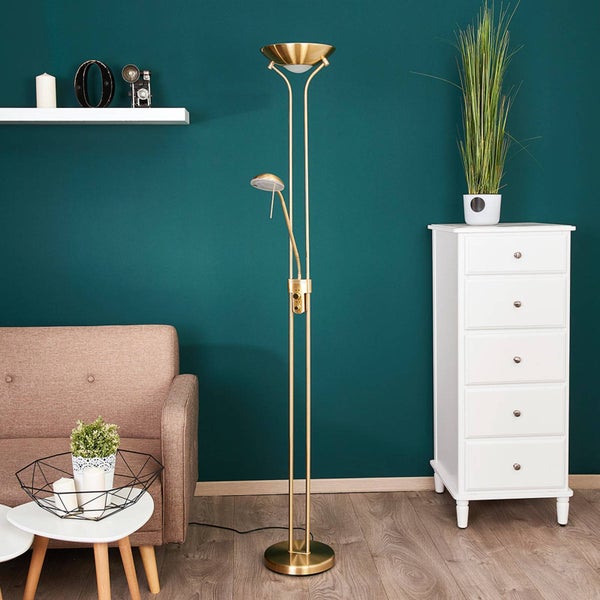 Goldfarbene Stehlampe mit Deckenfluter und verstellbarem Lesearm in einem modernen Wohnzimmer mit Sofa und Kommode.
