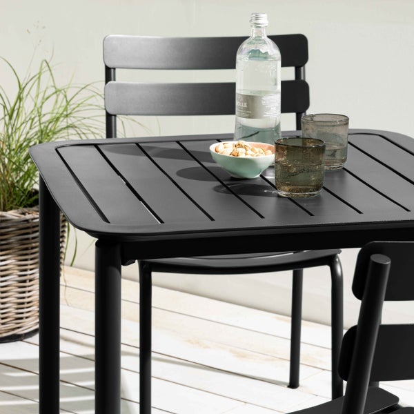 Moderner anthrazitfarbener Gartentisch aus Metall mit Lattenoberfläche und passenden Stühlen auf einer hellen Terrasse.
