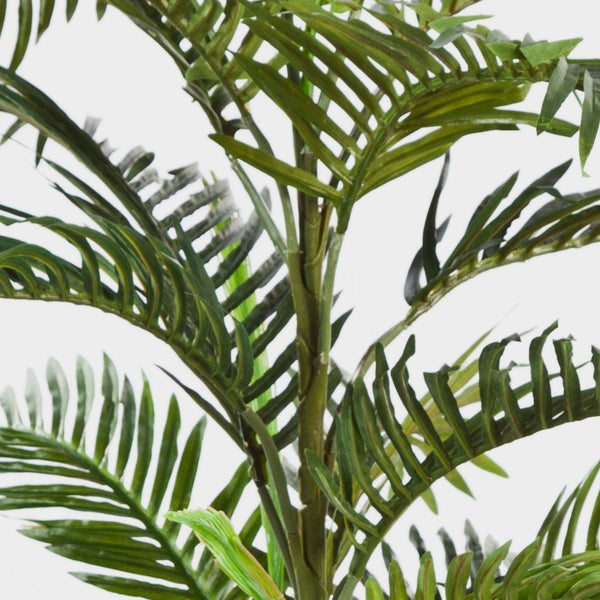 Nahaufnahme einer künstlichen Palme mit grünen Palmwedeln und strukturiertem Stamm.