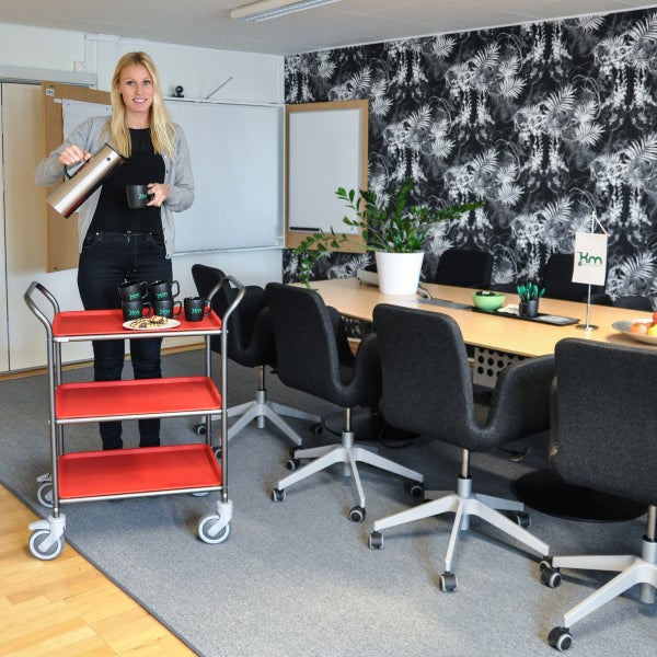 Eine Frau schenkt in einem Besprechungsraum Kaffee aus einer Thermoskanne in eine Tasse auf einem Servierwagen ein.