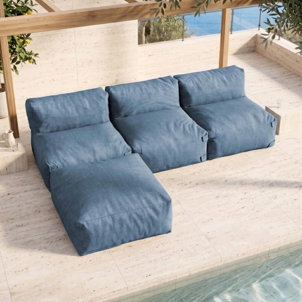 Modulares Outdoor-Sofaset mit blauem Stoffbezug und Hocker auf einer hellen Steinterrasse unter einer Holzpergola an einem Pool.