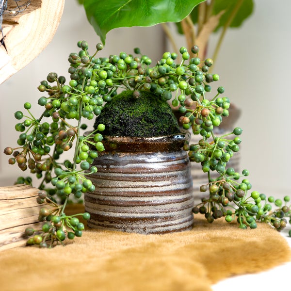 Dekorative Kunstpflanze mit Beeren in einem Topf.