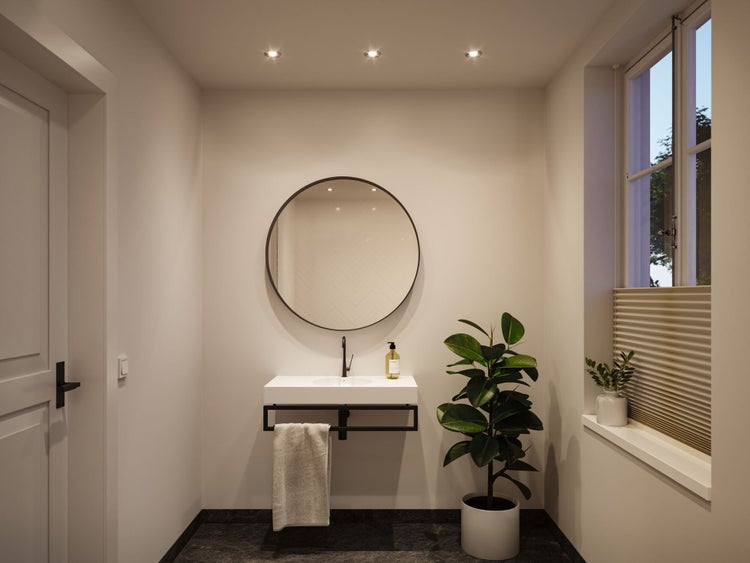 Modernes Badezimmer mit weißem Waschbecken, schwarzer Armatur, rundem Spiegel und Zimmerpflanze. Helles, minimalistisches Design mit Deckenspots.