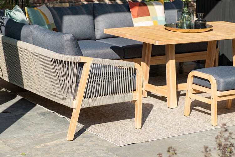 Garten-Lounge-Set aus hellem Holz mit Seilbespannung, grauen Polstern, einem Esstisch und einem Hocker auf einer Terrasse.