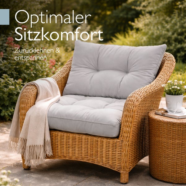 Heller Geflechtsessel für den Garten mit grauen Polstern, einer beigefarbenen Decke und passendem Beistelltisch auf einer Terrasse.