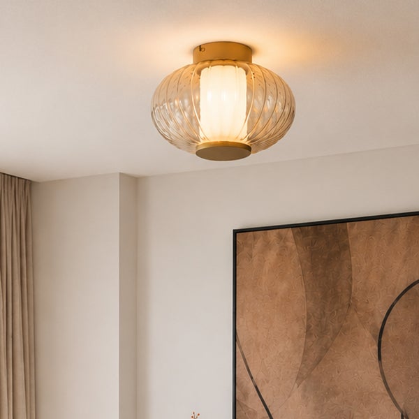 Moderne Deckenleuchte mit geriffeltem Klarglas und messingfarbener Halterung, montiert an einer hellen Decke.