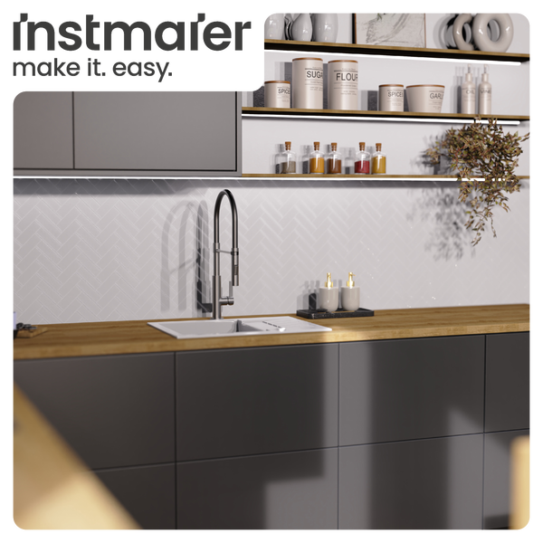 Helle, moderne Küche mit Hochbogenarmatur, weißem Spülbecken, Holz-Arbeitsplatte, dunkelgrauen Schränken und Fischgrät-Fliesen. Instmaier Logo.