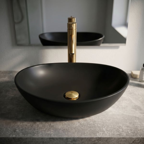 Modernes Badezimmer mit schwarzem Aufsatzwaschbecken, goldener Waschtischarmatur und passendem Ablaufventil auf einer Waschtischplatte in Steinoptik.