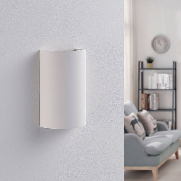 Weiße, gewölbte Wandleuchte aus Gips in einem modern eingerichteten Wohnzimmer mit Sofa und Regal.