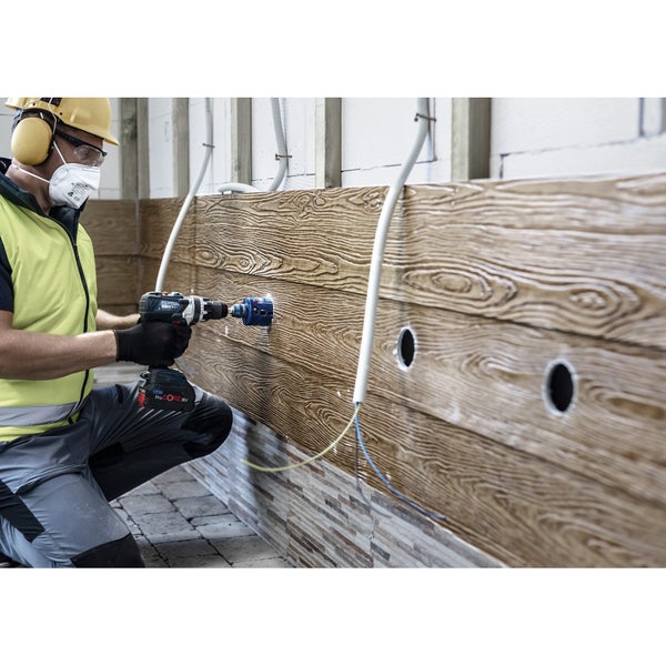 Handwerker bohrt mit einer Lochsäge ein Loch in eine Holzvertäfelung, wobei er Schutzkleidung trägt