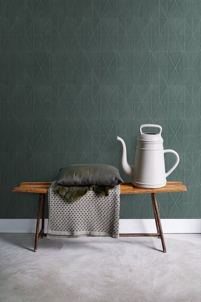 Dekorative Szene mit einer Gießkanne, einem Kissen und einer Decke auf einer Bank vor einer Wand mit geometrischem Muster