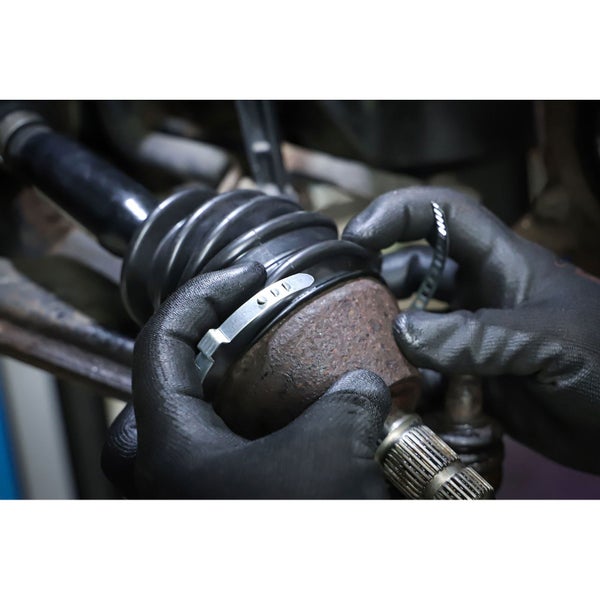 Detailaufnahme einer Antriebswelle mit Manschette, die von zwei Händen mit Schutzhandschuhen befestigt wird.