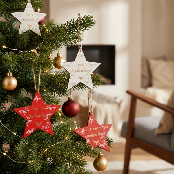Weihnachtsbaumschmuck in Sternform aus Holz mit weihnachtlichem Aufdruck und Aufhängung, dekoriert an einem künstlichen Tannenbaum.