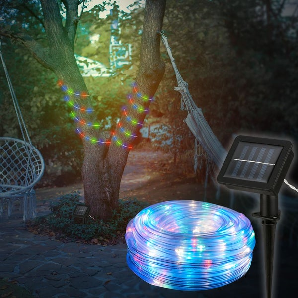 Bunter Solar-LED-Lichtschlauch für den Außenbereich, aufgerollt und um einen Baumstamm gewickelt im Garten, inklusive Solarpanel mit Erdspieß.