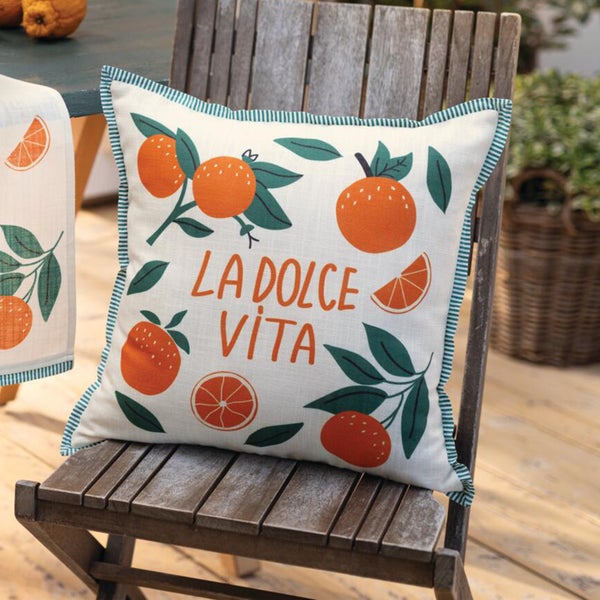 Dekokissen mit Orangenmotiv und dem Schriftzug La Dolce Vita auf einem Holzstuhl.