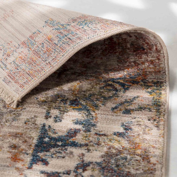 Nahaufnahme eines gewebten Teppichs mit Vintage-Muster, Fransen an der Kante und einer umgeschlagenen Ecke, die die Rückseite zeigt.