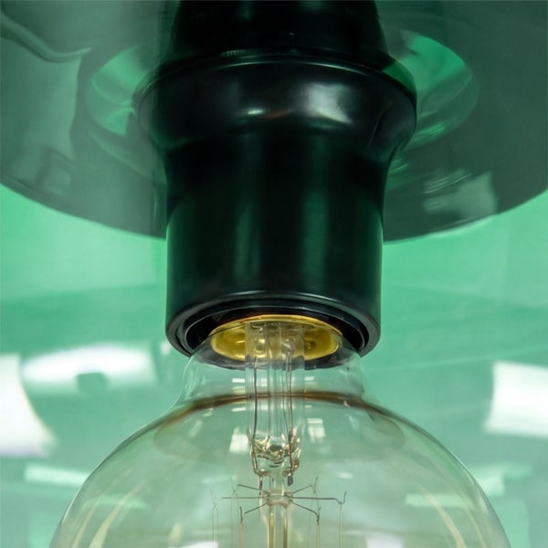 Detailaufnahme einer schwarzen Lampenfassung mit Glaskolben unter einem grünen Glasschirm.