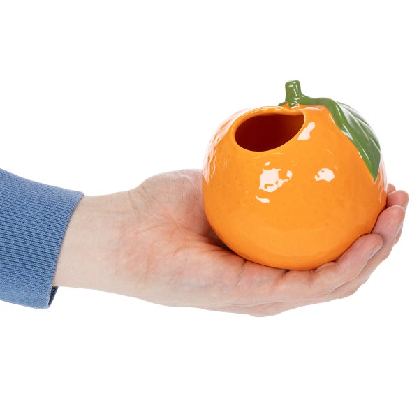 Eine Hand hält ein orangefarbenes Keramikgefäß in Form einer Orange mit einer Öffnung.