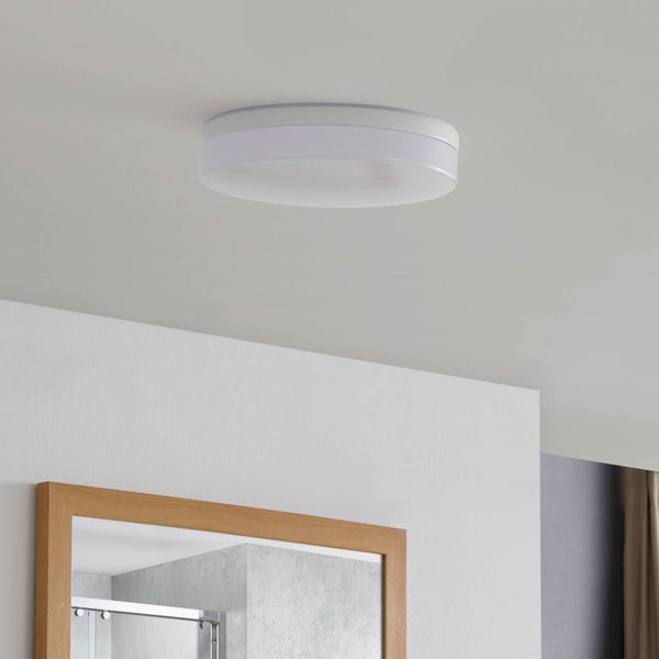 Runde weiße Deckenleuchte montiert an einer Decke über einem Spiegel mit Holzrahmen.