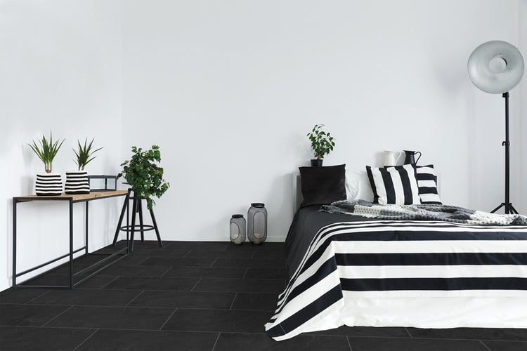 Schlafzimmer mit Bett, Stehleuchte und schwarzen Fliesen