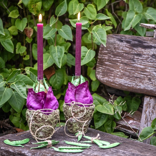 Zwei brennende, schlanke Kerzen in floralen Kerzenhaltern auf einem Holztisch