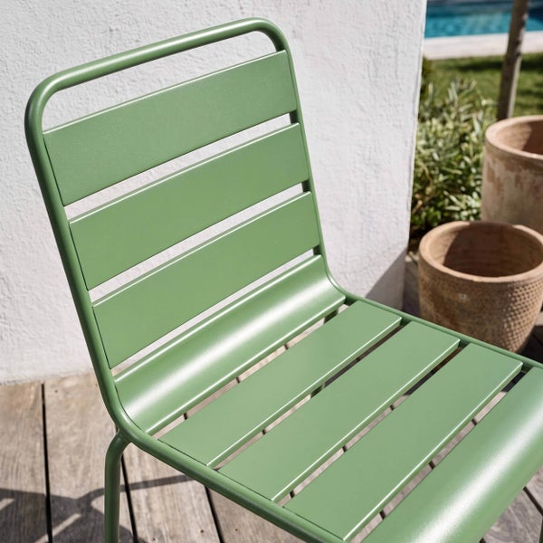Moderner grüner Gartenstuhl aus Metall mit Latten auf einer Holzterrasse neben Terrakotta-Töpfen in einer hellen Umgebung.